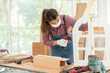 © godji10 - A confident young female carpenter uses a hand drill to assemble the wood window in the carpentry shop. Asian handywoman apprentice working in a workshop. DIY woodworking crafts and Hobbies concepts.