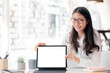 © NAMPIX - Portrait of young asian woman with glasses showing blank screen of tablet while sitting at office desk.