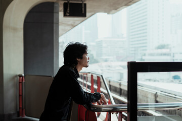 Side view of a man looking at city on sky train platform.