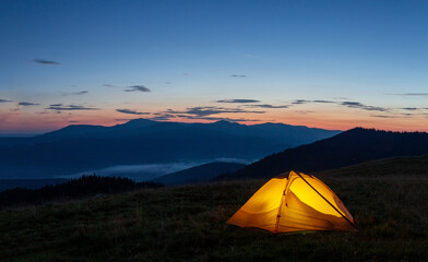 Wall Mural - orange luminous tent on the mountain in evening or early morning
