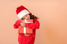 Cute Little Girl In Santa Hat And With Gift On Color Background