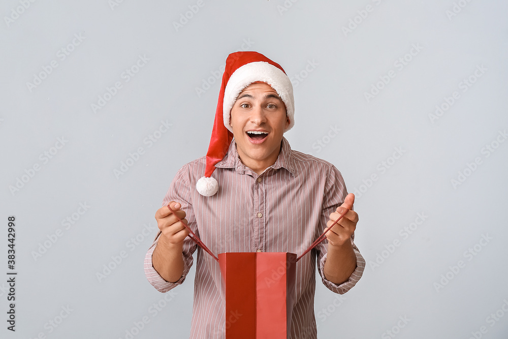 Surprised man in Santa hat and with shopping bag on grey background