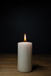 © Angela Rohde - A white burning candle on a wooden table, dark background and copy space