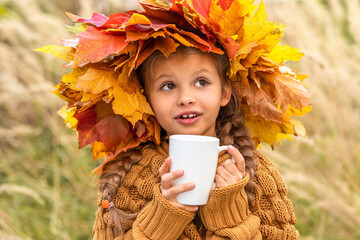 Wall Mural - On a bright autumn day, a little girl drinks a hot drink.