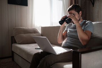 funny man looking searching binoculars a laptop on the table working at home office.