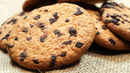 American chocolate chip cookies on a brown wooden table and on a linen napkin close-up. Traditional rounded crunchy dough with chocolate chips. Bakery. Delicious dessert, pastries. Rural still life.