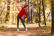 © junky_jess - Warm up before jogging. Caucasian adult woman in red sportswear and a cap does side bends in the forest in autumn outdoor, selective focus