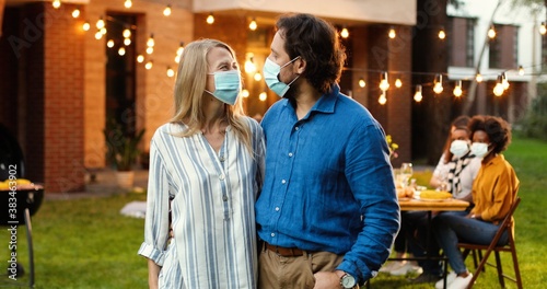 Fotografía Portrait of Caucasian middle-aged couple in medical masks hugging in yard at picnic