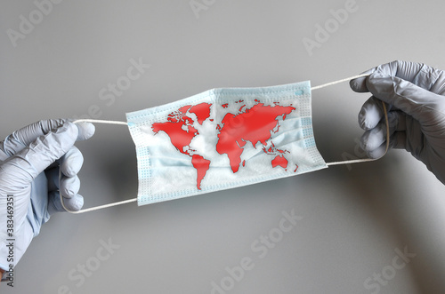 the doctor\'s hands protected by blue gloves hold a blue surgical mask with world map. Covid-19 epidemic around the world. Concept of coronavirus disease and world crisis.