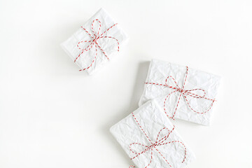 Christmas / New year background. Minimal festive holiday composition. Three gifts wrapped in white paper with red and white rope on white table. Flat lay, top view, copy space.