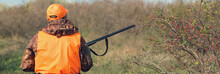 Duck Hunter With Shotgun Walking Through A Meadow.