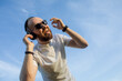 © kalinichenkod - portrait of a handsome young man with beard listening music with headphones against a cloudy sky background