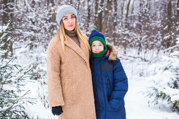 Portrait of happy mother with child son in winter outdoors. Snowy park. Single parent.