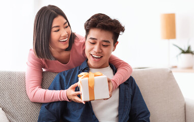 Wall Mural - Chinese Girlfriend Giving Gift Box To Surprised Boyfriend At Home