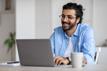 Poster - Smiling Indian Writer Using Laptop Computer, Sitting At Desk In Home Office
