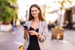 © F8  \ Suport Ukraine - Smiling woman walks down the central city street and uses her phone. Pretty summer woman walks down the street looking at her mobile phone