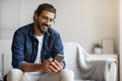 Fotomural Handsome young indian guy sitting with smartphone at home, messaging with friend