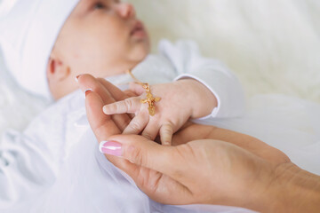 The sacrament of the baptism of a child. The kid is holding a cross. Selective focus.