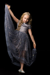 Wall Mural - A little girl in a long, elegant dress of a princess on a black background.