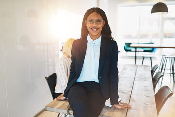 Wall Mural - Smiling African businesswoman sitting on a table