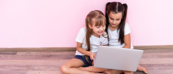 Two little girls sitting in front of a laptop and laughing, close-up, positive emotions, entertainment on the Internet for children