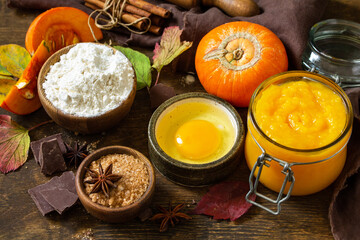 Wall Mural - Seasonal food background - ingredients for autumn baking (pumpkin puree, eggs, flour, chocolate, sugar and spices) on a wooden table.