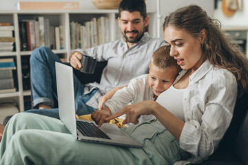 Wall Mural - young family sitting on sofa and using laptop computer at home