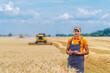 © Vadim - Young attractive farmer standing in wheat field. Combine harvester working in wheat field in background.
