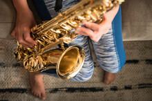 Close Up Of Young Girl Sitting On Brown Couch Practicing Saxophone