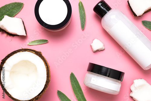 Natural organic eco cosmetics with coconut oil. Cosmetic containers with cream and lotion, broken coconut, green leaves on pink background flat lay top view. Beauty SPA branding mock-up. Blank label