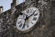 Relógio no topo de uma torre em pedra datado de 1913 com um candeeiro posicionado ao centro, horas descritas em numeração romana, de de fundo, medieval 