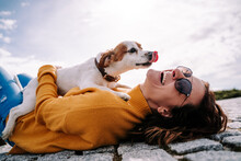A Beautiful Woman Laughing While Her Pet Is Licking Her Face In A Sunny Day In The Park In Madrid. The Dog Is On Its Owner Between Her Hands. Family Dog Outdoor Lifestyle