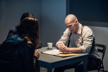 In the interrogation room, the investigator and the officer are talking to the criminal.