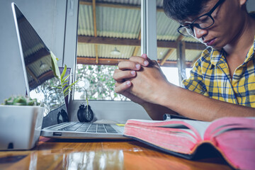 Wall Mural - Young man with glasses sitting praying in front of computer laptop, Online church in home, Home church during quarantine coronavirus Covid-19, Religion concept.