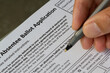 Hand holding a pen and filling out a New York State Absentee Ballot Application form. Selective focus on the form.