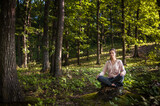 Fototapeta  - Young woman wearing yoga pants meditating in the woods on a sunny morning.