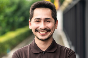 Young man asian smiling and looking at camera. Portrait of a happy handsome young man in a  urban street. Close up face of young cool trendy man looking at camera