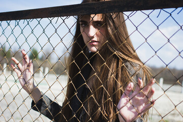 Shot through metal net fence  of beautiful girl with strong sight