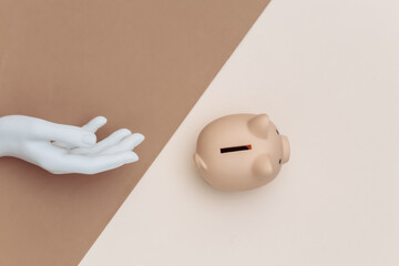 Wall Mural - Piggy bank and mannequin hand on brown beige background. Flat lay minimalism. Top view.