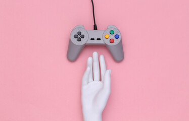 Poster - Mannequin hand touching retro gamepad on pink background. Top view. Creative art, minimalism