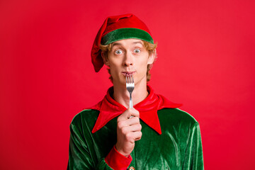 Wall Mural - Photo of funky elf guy lick fork x-mas christmas spirit meal concept wear green headwear isolated on red shine color background.