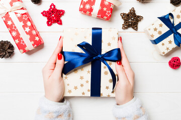 Top view of a woman holding a gift box in her hands on festive wooden background. Christmas decorations. New year time concept