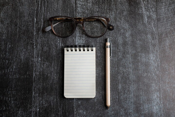 Wall Mural - staionery scene. open notebook pencil and stylish glasses on black wooden background. flat lay top view