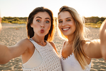 Two young caucasian women smiling and taking selfie photo on beach