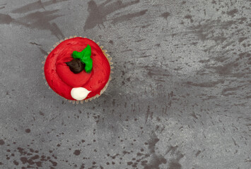 Wall Mural - Top view of a brightly frosted red cupcake on a gray mottled background.