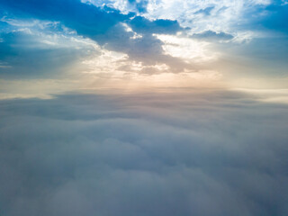  Aerial drone flight over the fog. There are thick clouds of fog below, the sun breaks through the clouds.