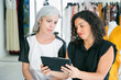 © Mangostar - Focused customer and shop assistant meeting in fashion store, sitting together and using tablet, discussing clothes and purchases. Consumerism or shopping concept