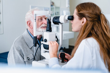 Wall Mural - Female ophthalmic doctor diagnosing elderly patient`s sight using ophthalmic equipment