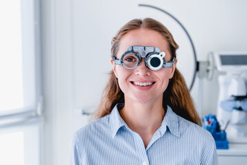 Wall Mural - Smiling young female patient checking up sight using ophthalmic glasses