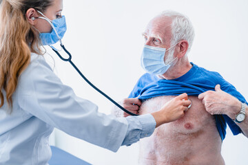 Cropped photo of senior male patient wearing mask being examined by woman doctor in mask isolated over white background